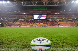 Stock Photo. Gilbert Super Rugby ball on grass with goal-posts and stadium lights